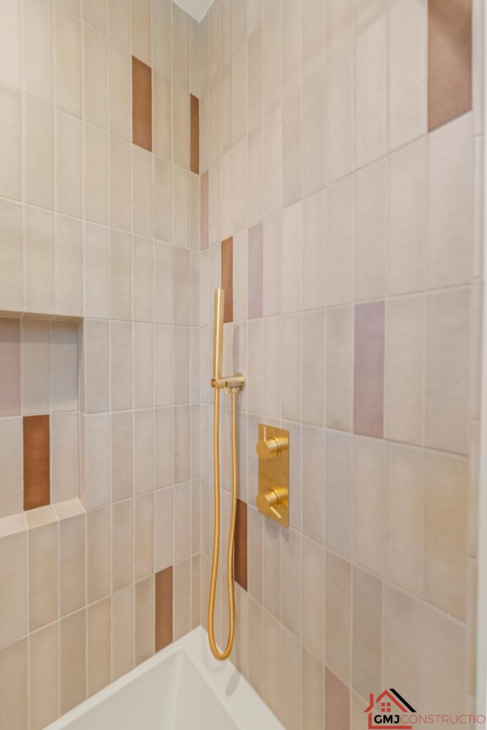 Tub-shower detail with warm neutral tile and gold-toned fittings
