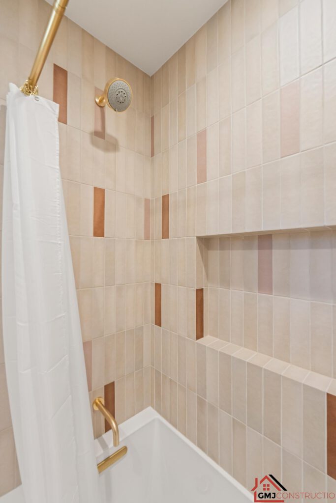 Gold-toned tub-shower fittings against a varied warm neutral tile pattern