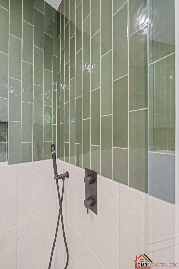 Dark shower controls and handheld sprayer against green and pale tile
