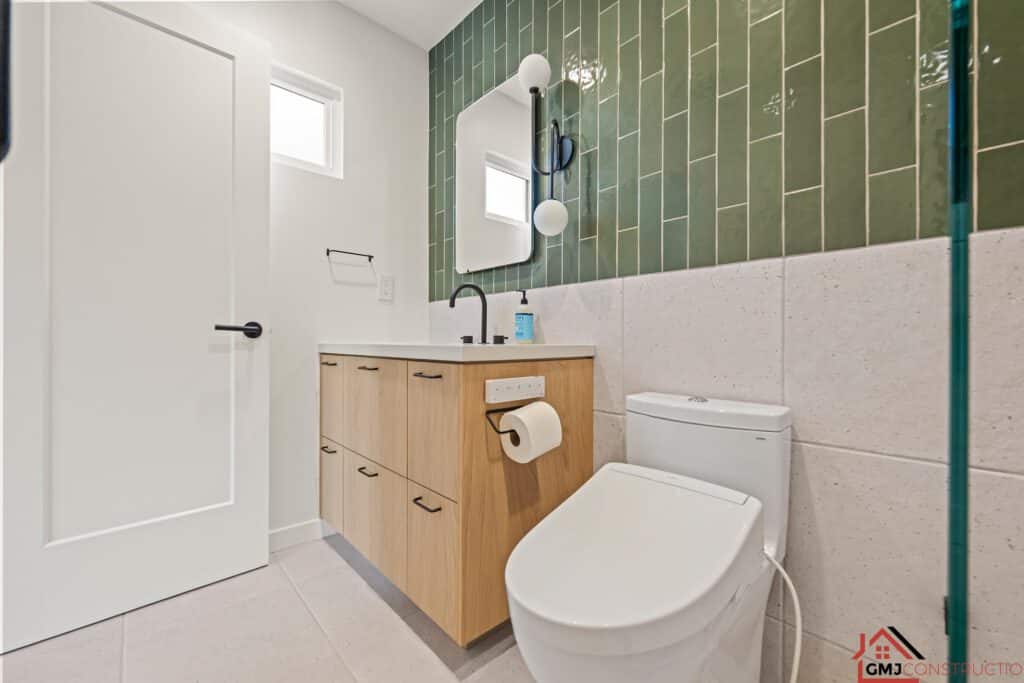 Wood bathroom vanity, rounded rectangular mirror and green-tiled wall