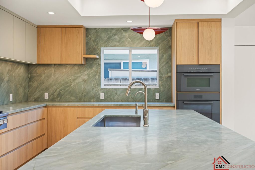 Kitchen island sink, green-veined countertop and built-in ovens at Samson Way