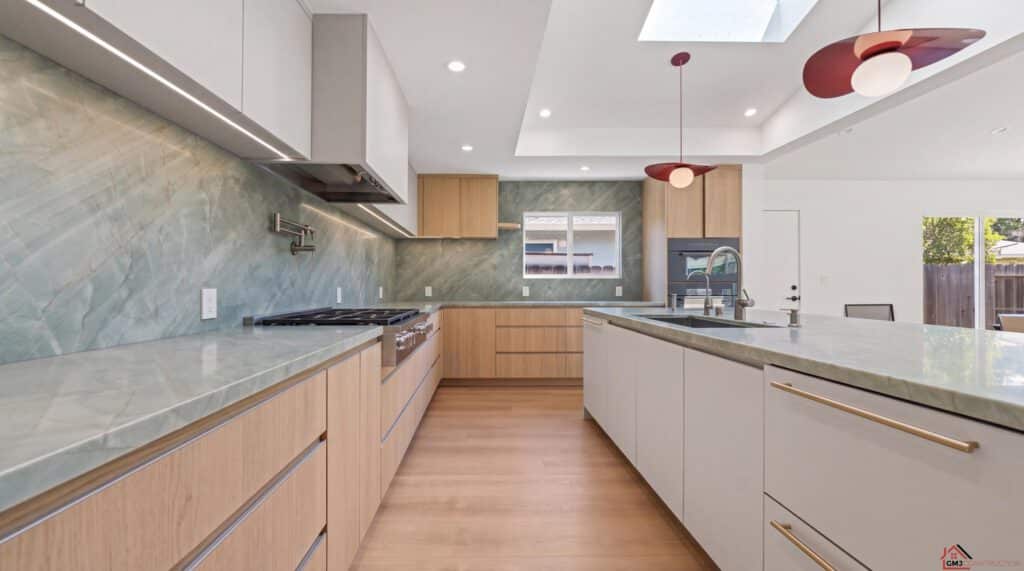 Wide kitchen view with green-veined counters, wood cabinetry and sculptural pendants